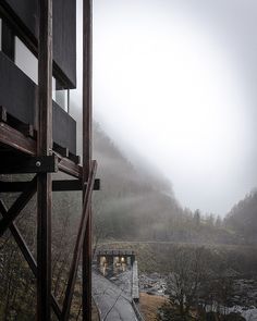 an open door leading to a wooden walkway in the foggy mountains with trees on both sides