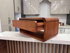 a wooden object sitting on top of a white counter in a kitchen next to cabinets