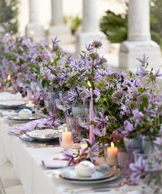 a long table is set with purple flowers and candles for an elegant dinner or party