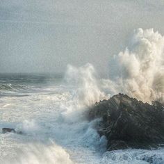 an ocean wave crashing over a rock in the middle of the ocean with white foam on it