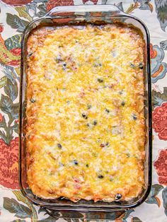 a casserole dish with cheese and other toppings on a floral table cloth