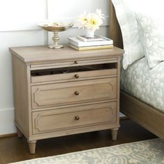 a nightstand with two drawers and a book on top of it next to a bed