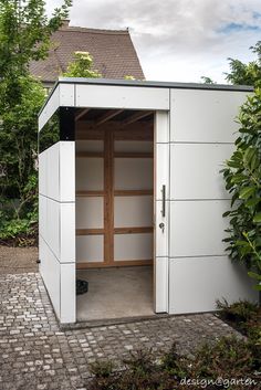 an outhouse with the door open on a brick walkway in front of some trees