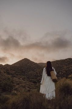 a woman is walking up a hill with her back to the camera as the sun sets