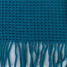 a blue knitted blanket with fringes on it