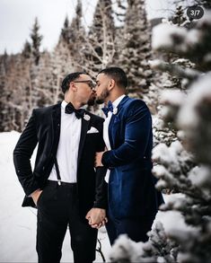 two men in tuxedos standing next to each other near snow covered pine trees