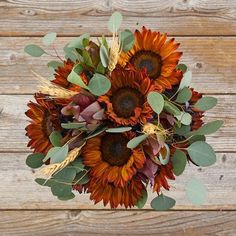 a bouquet of sunflowers and eucalyptus leaves on a wooden surface