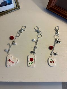 three key chains with charms attached to them sitting on a table next to a framed photo