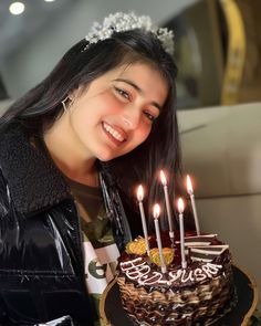 a woman smiles as she holds a cake with lit candles on it in front of her