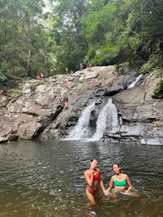 two women are in the water near a waterfall