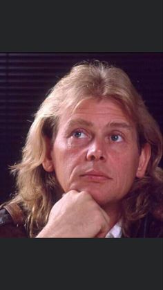 a man with long blonde hair and blue eyes stares into the distance while wearing a leather jacket