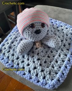 a crocheted teddy bear sitting on top of a blue and white square blanket