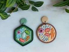 two wooden earrings sitting next to each other on top of a white surface with green leaves