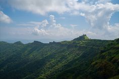 the mountains are covered in green grass and blue skies with white clouds above them on a sunny day