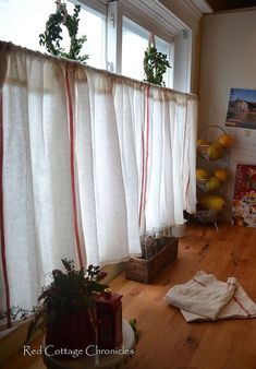 a room with wooden floors and white drapes on the window sill, next to some fruit