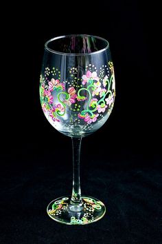 a wine glass with flowers painted on the bottom and sides, sitting on a black surface