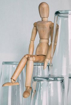 a wooden doll sitting on top of two glass vases next to an empty bottle