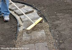 a person with a broom is sweeping up the dirt in front of a brick walkway