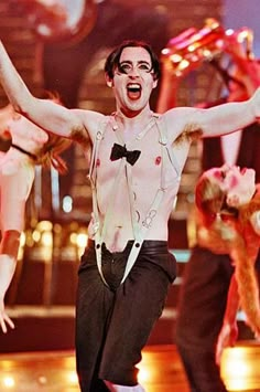 the man is dancing on stage with his hands in the air and other dancers behind him