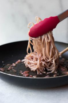 someone is using a red spatula to stir noodles in a skillet on the table