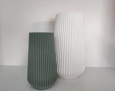 two white and green vases sitting next to each other on top of a table