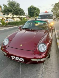 a red sports car parked on the side of the road next to a white van