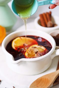 a person pouring liquid into a bowl filled with fruit and spices next to spoons