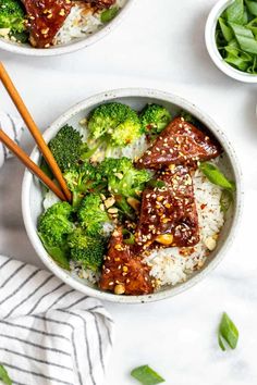 two bowls filled with rice, broccoli and beef on top of a table