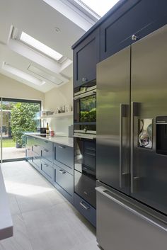 a stainless steel refrigerator in a kitchen with skylights on the ceiling and windows above it