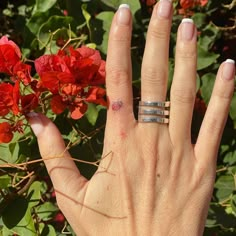 a woman's hand with two rings on it and red flowers in the background