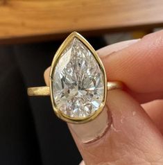 a woman's hand holding a yellow gold ring with a pear shaped diamond