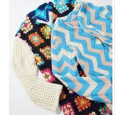 three knitted sweaters are laying next to each other on a white surface, one is blue and the other has multicolored flowers