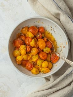 a white bowl filled with tomatoes on top of a table next to a napkin and spoon