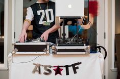 a man standing next to a dj set up on top of a white cloth covered table