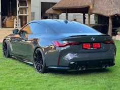 the rear end of a gray bmw car parked on grass in front of a house