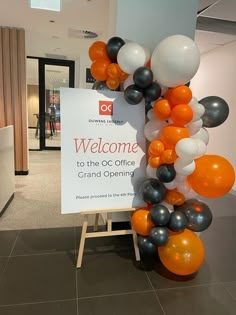 an orange and black welcome sign surrounded by balloons in the lobby at a corporate office