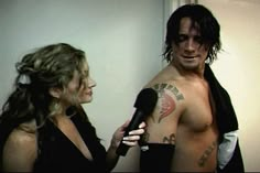 a shirtless man holding a microphone next to a woman with tattoos on her chest