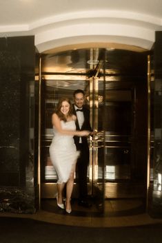 a man and woman in formal wear are exiting an elevator together, dressed in white