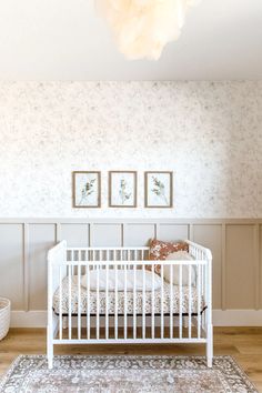 a white crib in the corner of a room with two pictures on the wall