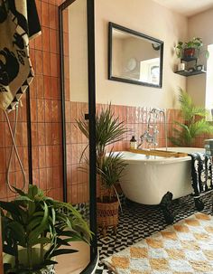 a bath tub sitting in the middle of a bathroom next to a mirror and potted plants