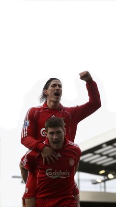 two men in red soccer uniforms are on top of each other and one man is holding his arms up