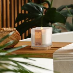 a white candle sitting on top of a wooden table next to a potted plant