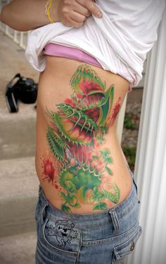 a woman is showing off her colorful tattoo on her stomach and back, while standing in front of a building