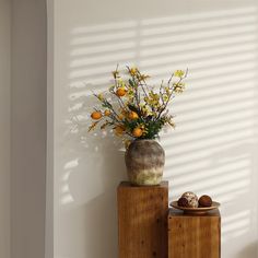 a vase filled with yellow flowers sitting on top of two wooden boxes next to a wall