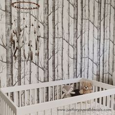 a white crib with a teddy bear in it next to a forest wallpaper