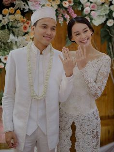 a man and woman standing next to each other in front of a flower covered wall