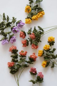 small crocheted flowers laid out on a white surface with green stems and yellow ones