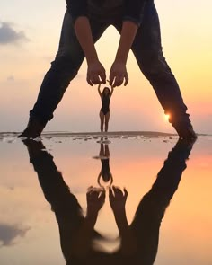 a person bending over to touch the water with their reflection on the ground at sunset