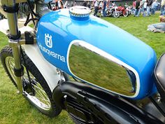 a blue and white motorcycle parked on top of a lush green field next to people