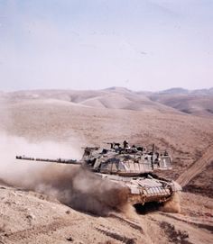 an army tank driving through the desert with dust coming out of it's tires